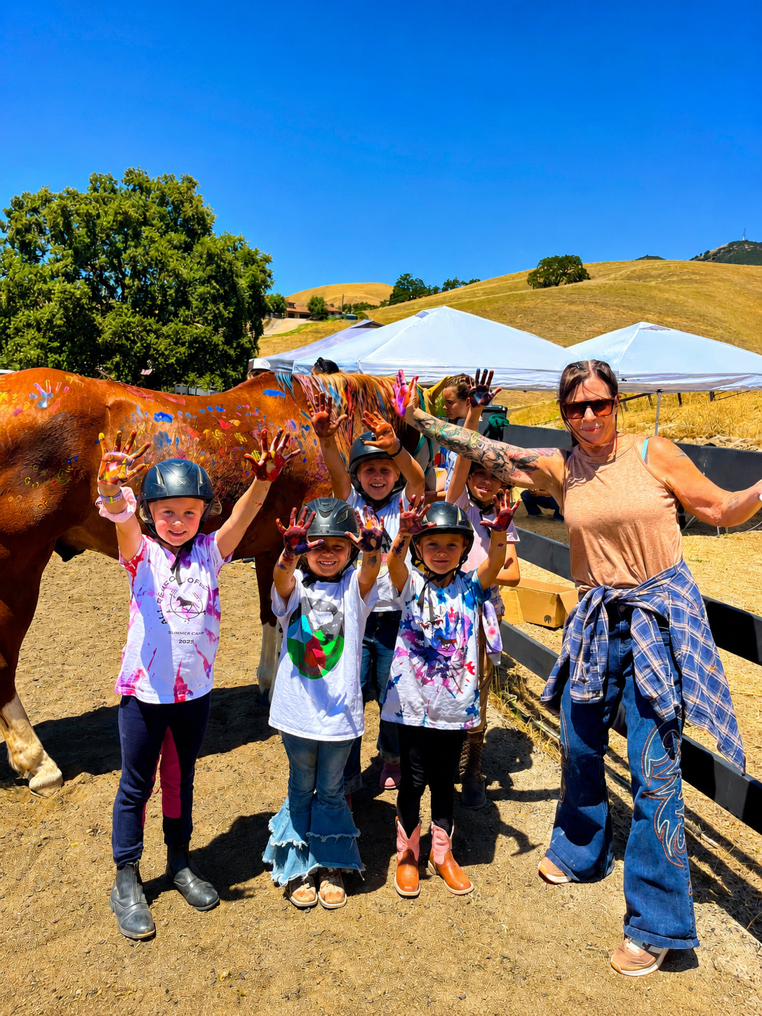 Kids and instructor with paint-covered hands next to a horse painted with colorful handprints at summer camp