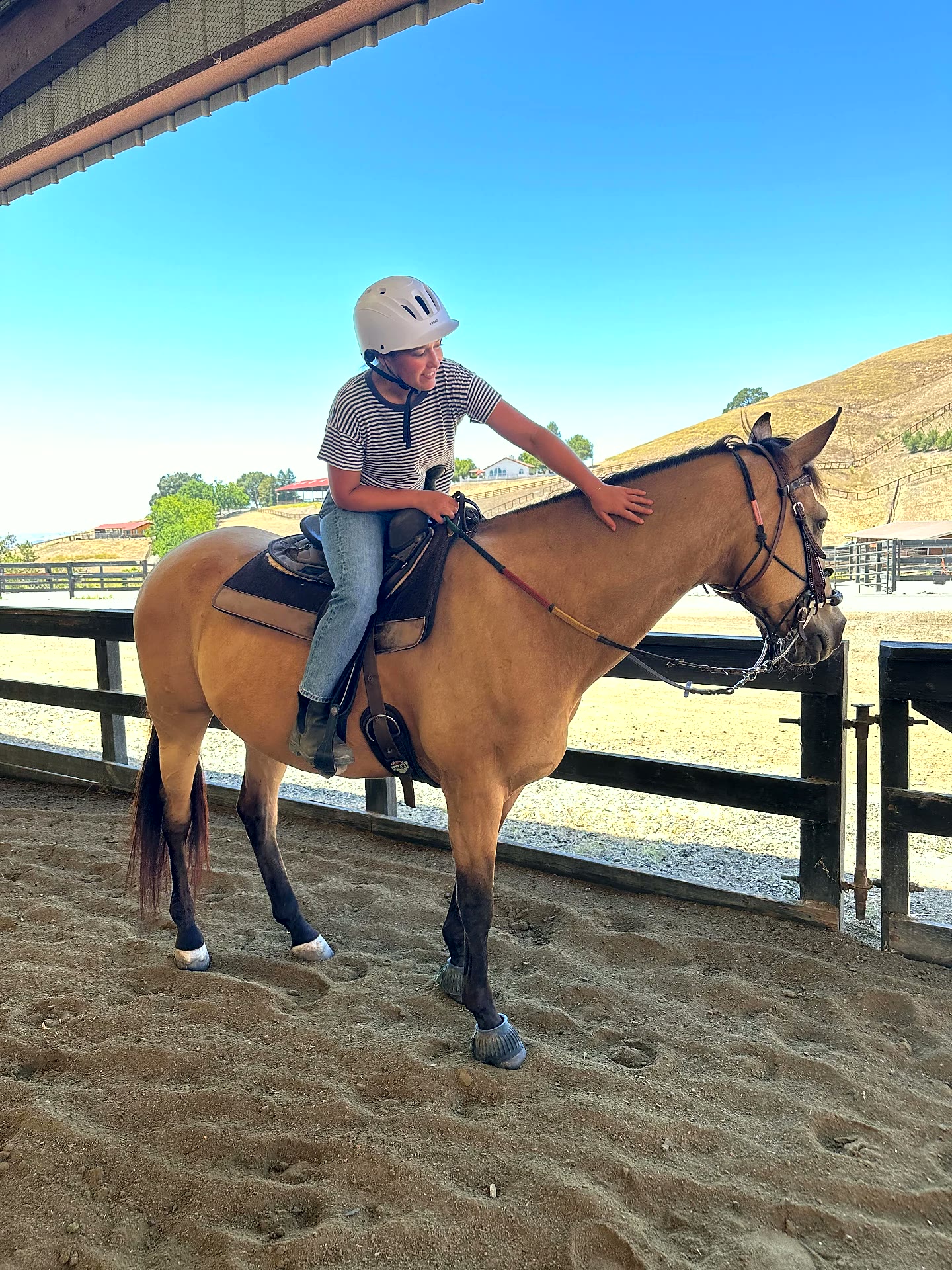 Rider leaning forward to pat her buckskin horse's neck during a lesson