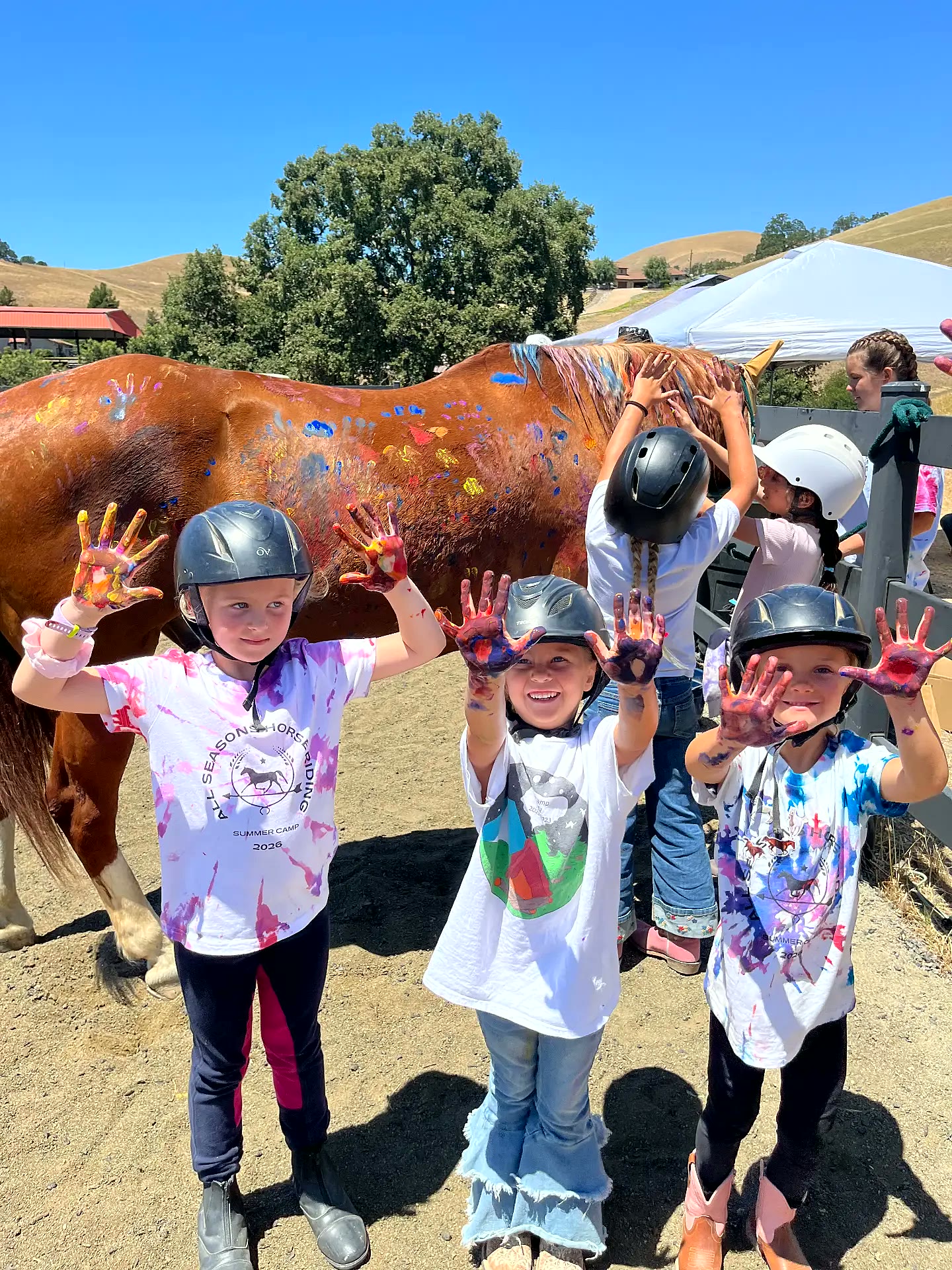 Summer camp kids showing off paint-covered hands beside a painted horse